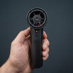 Studio photo of the AirBlaster Pro held in hand, showing the front view with the power button, indicator light, and nozzle mounting port.